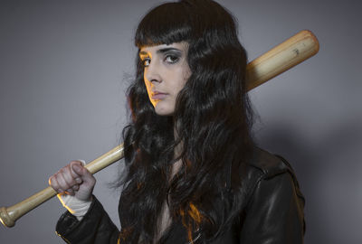 Portrait of young female model holding baseball bat against gray background