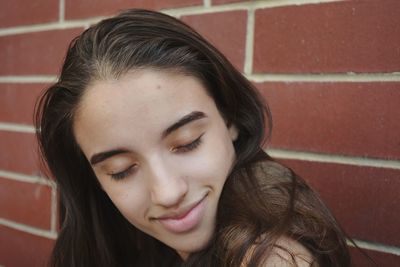 Close-up of smiling woman with eyes closed against brick wall