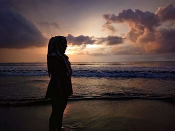 Woman standing on beach against sky during sunset