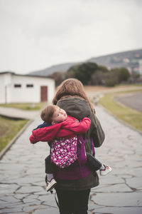 Rear view of mother carrying son wile walking on walkway