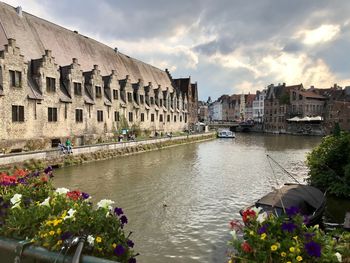 View of buildings by river against cloudy sky