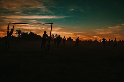 Silhouette people playing soccer against sky during sunset