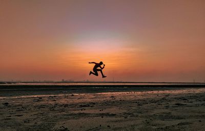 Silhouette man jumping on beach against sky during sunset