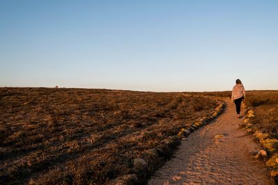 Rear view of woman walking on field against clear sky