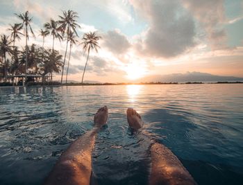 Scenic view with foot floating on sweming pool of sea against sky at sunset