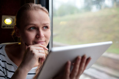 Smiling woman using digital tablet while sitting in train