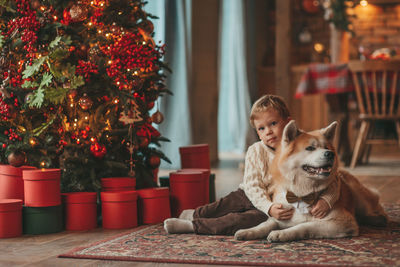 Candid authentic happy little boy in knitted beige sweater hugs dog with bow tie at home on xmas