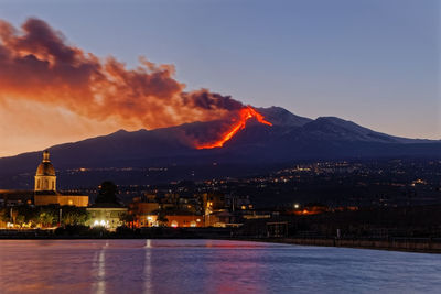 Illuminated buildings in the city during etna eruption