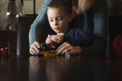 Midsection of mother assisting son in making toy blocks at table