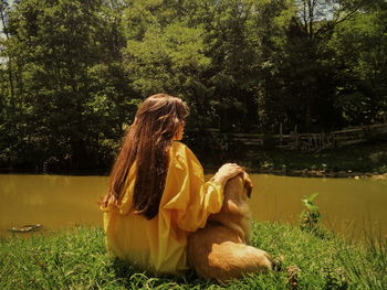 Woman with dog sitting on grass against trees