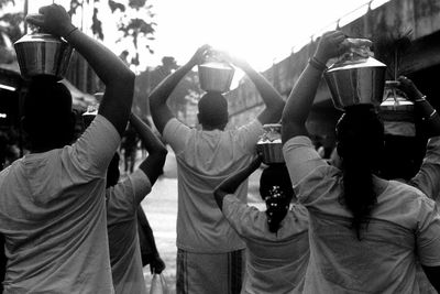 Rear view of people carrying religious pots on head while walking on street