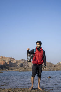 Full length of man standing on rock in sea against clear sky