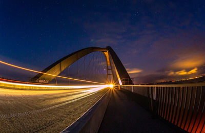 Light trails on bridge against sky at night