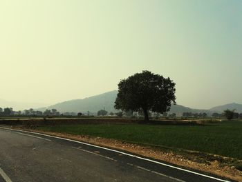 Road passing through field against clear sky