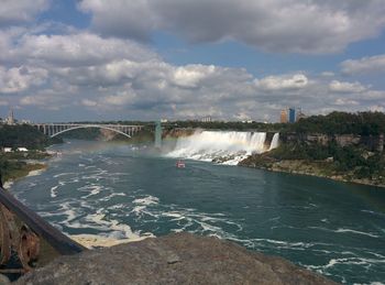 Scenic view of waterfall against cloudy sky