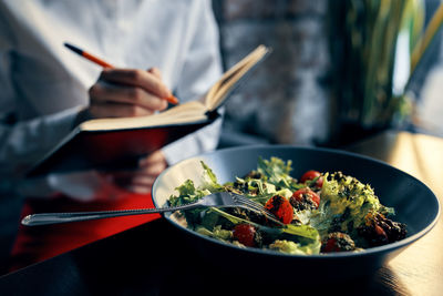 Midsection of chef writing in diary in front of food in plate