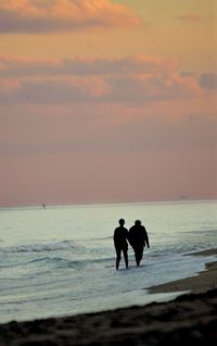 Silhouette friends standing on beach against sky during sunset