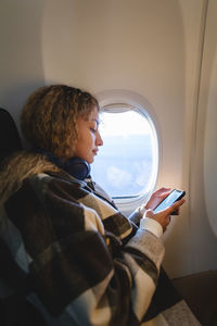 Woman using smart phone sitting near window in airplane