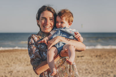 Portrait of young woman and baby smiling at beach