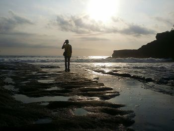 Rear view of man standing at beach against sky during sunset