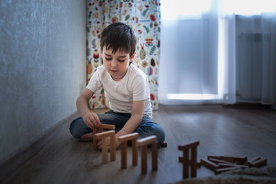 Boy caucasian brunette sad and serious plays on the floor, builds towers from wooden designer, 