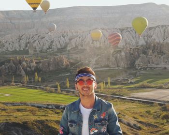 Portrait of young man with sunglasses standing on mountain against hot air balkona in cappadocia