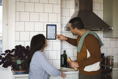 Girl looking at father using home automation device in kitchen at home