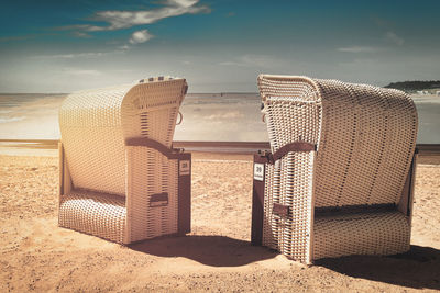 Hooded chairs on beach against sky