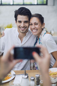 Friend photographing couple through smart phone in cafe