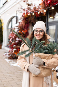 A stylish young woman wearing a hat with branches of nobilis in a bag walks around the christmas 