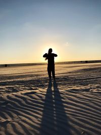 Man standing on snowy field against sky during sunset