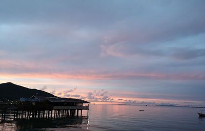 Silhouette house by sea against sky at sunset