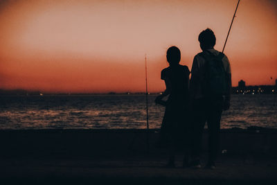 Silhouette men standing at beach against sky during sunset