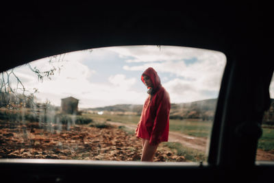 Young woman standing on land seen through car window