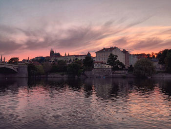 Buildings by river against sky at sunset
