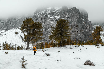 Rear view of female hiker walking on snowy path under amazing misty mountains