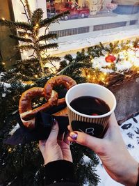 Midsection of woman holding coffee cup by christmas tree