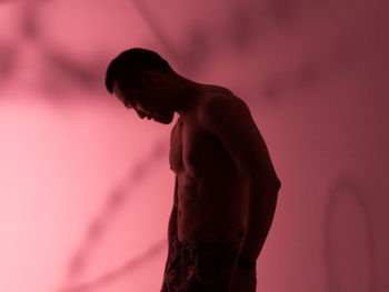 Side view of shirtless man standing against pink wall