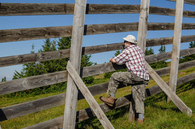 Full length of man sitting on wood against sky