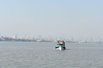 Nautical vessel on sea by buildings against clear sky