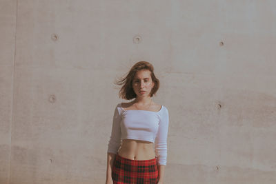 Portrait of young woman standing against wall