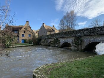 Arch bridge over river by buildings against sky