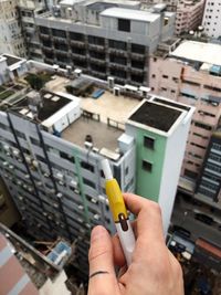 Midsection of person holding mobile phone against buildings in city