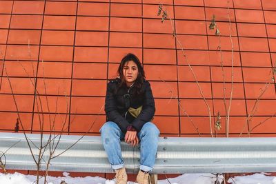 Portrait of teenage girl sitting against brick wall