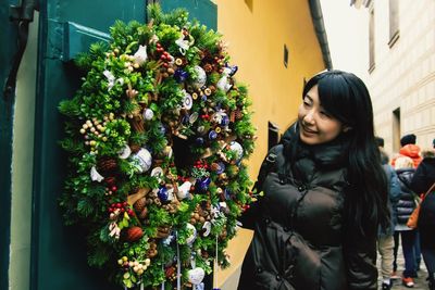 Smiling young woman looking at wreath during winter