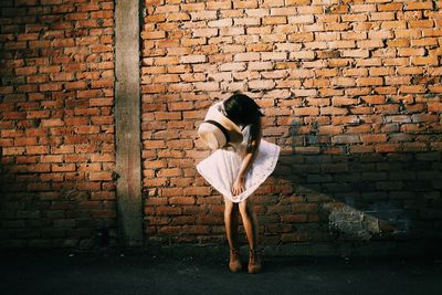 Woman holding dress and sunhat while standing against brick wall