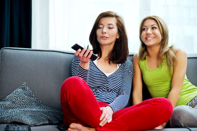 Sisters watching tv while sitting on couch at home 