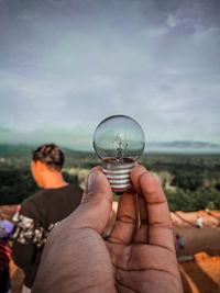 Midsection of person holding glass of water against sky