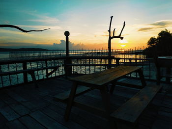 Silhouette chairs and table by sea against sky during sunset