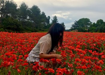 Side view of woman with red flowers on field